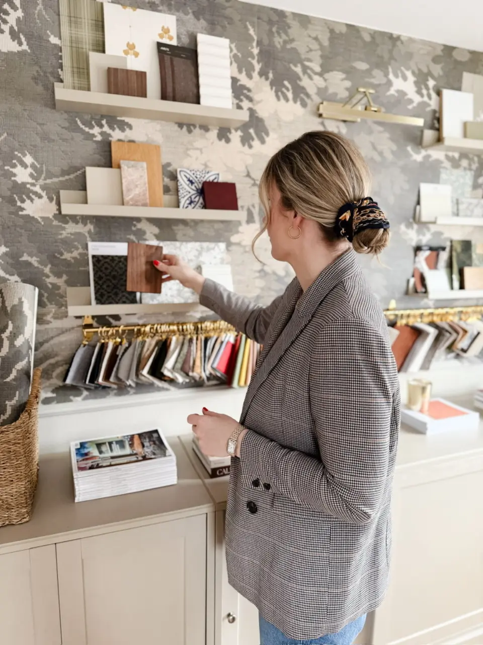 Nora, Gründerin von Studio Olivia Interior, wählt im Studio ein Holzfurnier-Muster vor dem Material- und Musterregal aus