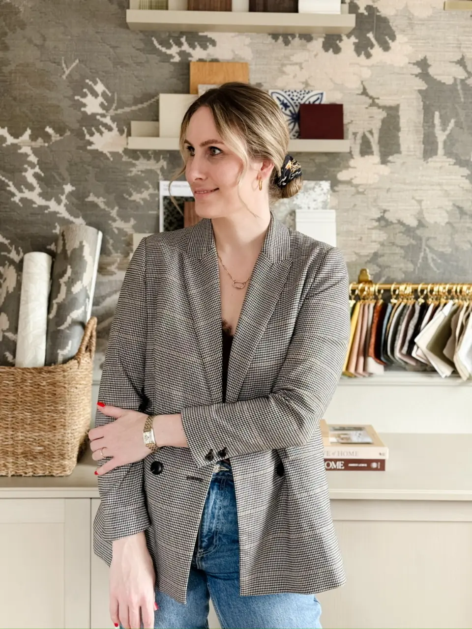 Nora, Gründerin von Studio Olivia Interior, im Karo-Blazer vor einer Wand mit Tapeten- und Stoffmustern in ihrem Studio